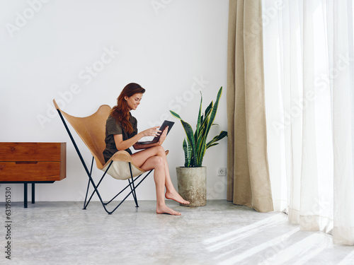 Woman sitting in a chair with a laptop watching a movie and social media at home smile, modern stylish interior Scandinavian lifestyle, copy space.