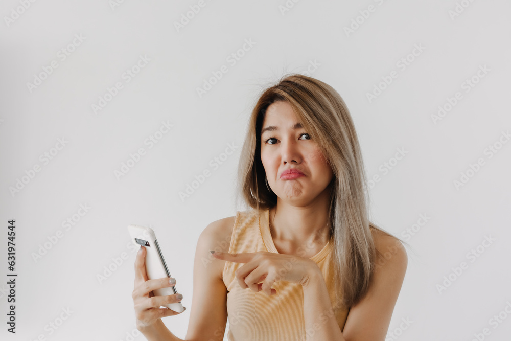 Boring and disappointed asian women wear yellow top pointing finger at mobile, isolated over white background wall. Boring and disappointed asian women wear yellow top pointing finger at mobile, isolated over white background wall.