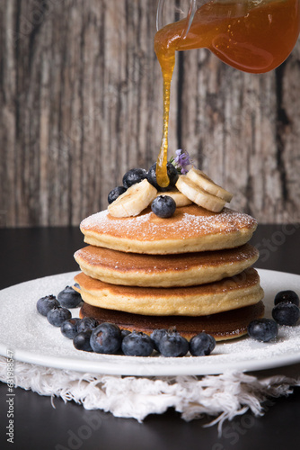 Pancakes stack with banana and blueberries topping and bee honey breakfast food