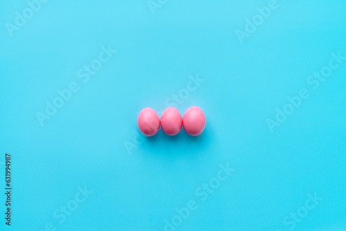High angle view of three bright pink eggs prepared for Easter celebration lying on center of turquoise surface 