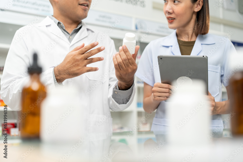 Two asian man and woman professional Pharmacist colleagues working at drugstore pharmacy. Asking the questions of medication standing near pharmacy shelves counter with medicines Two asian man and woman professional Pharmacist colleagues working at drugstore pharmacy. Asking the questions of medication standing near pharmacy shelves counter with medicines
