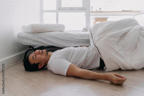 Asian man falling down from the bed lying on the floor at home.