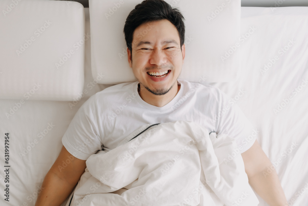 Happy smiling asian man lie down on white bed. Happy smiling asian man lie down on white bed.