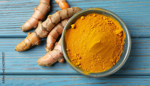 Bowl with turmeric powder and raw roots on blue wooden table, flat lay