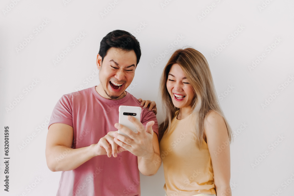 Happy asian couple lover laughing at the news content in the smartphone isolated on white. Happy asian couple lover laughing at the news content in the smartphone isolated on white.