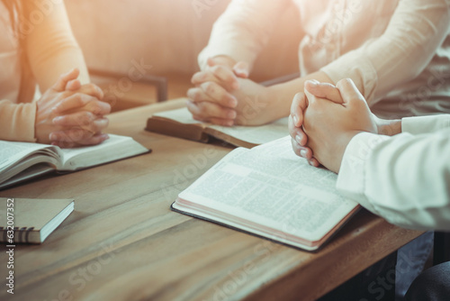 group of christian  sitting around wooden table with open blurred bible page and praying to God together