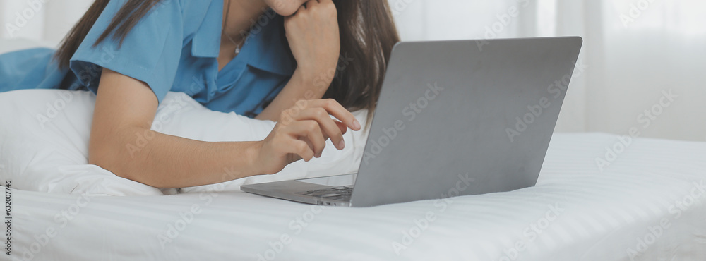 Naklejka premium Young Asian woman with beautiful face, long hair, blue shirt lying on bed in white bedroom at home with cup of coffee and video call with laptop talking to relatives on vacation. holiday concept.