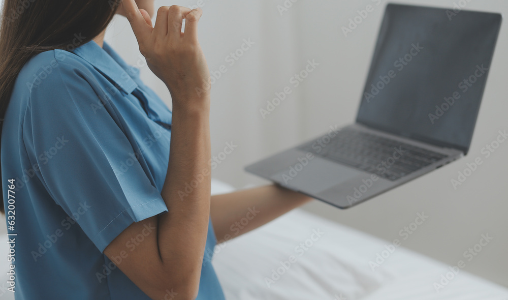 Obraz premium Young Asian woman with beautiful face, long hair, blue shirt lying on bed in white bedroom at home with cup of coffee and video call with laptop talking to relatives on vacation. holiday concept.