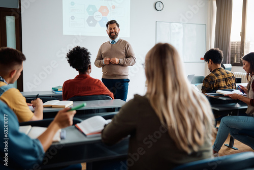 Happy mature teacher talks to his students while holding presentation in lecture hall.