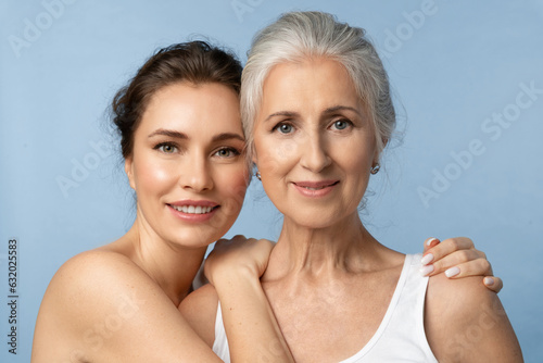 Smiling woman hugs joyful elderly mother by the shoulders. Beauty portrait of beautiful women of two generations, focus on alderly woman.