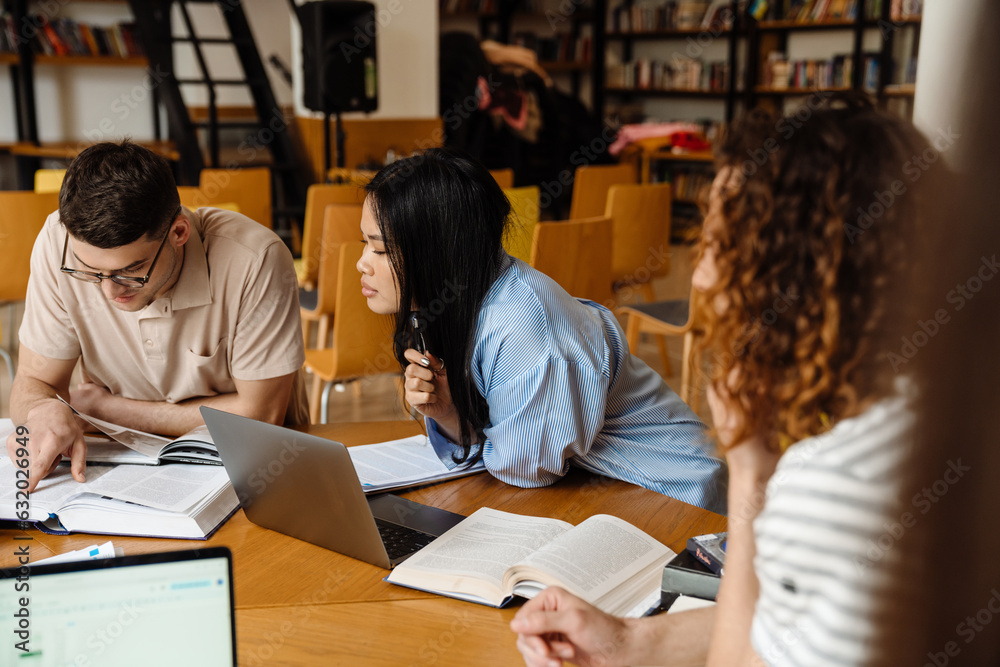 Group of multiethnic students preparing for exams together while sitting in library Group of multiethnic students preparing for exams together while sitting in library