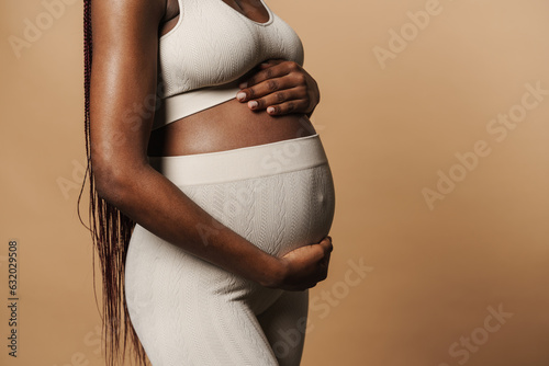 Sideview of african pregnant woman standing and holding her belly