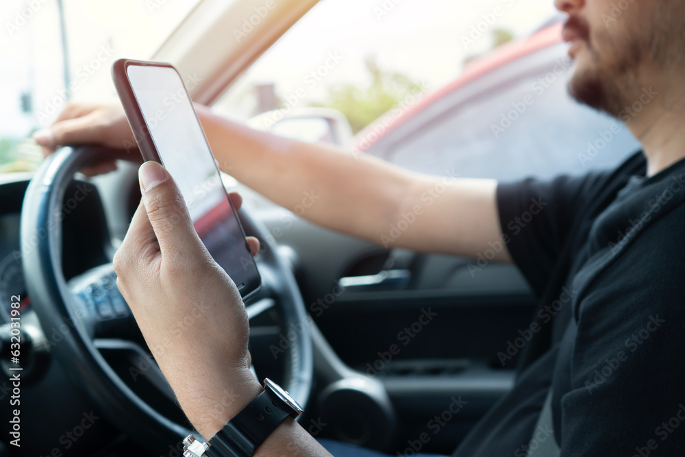 Young man reading messages holding a cell phone while driving. Dangerous behavior, accident risk.