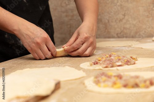 A woman prepares pies from dough and minced meat on the table