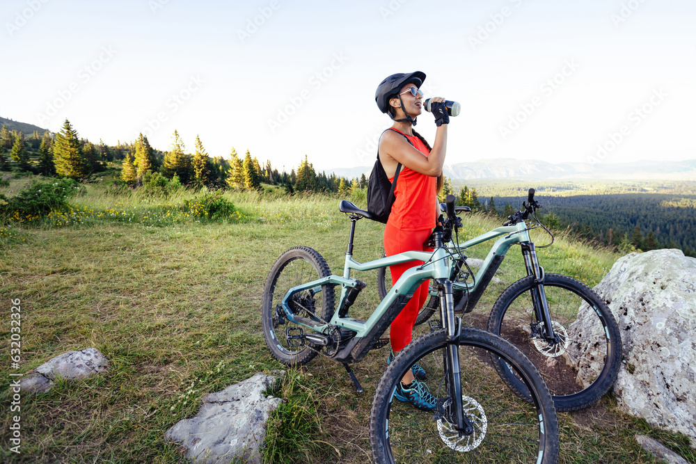 Fototapeta premium Cyclist woman standing with bike and drinking water