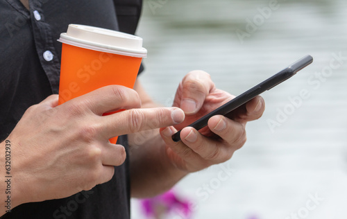 Phone with coffee in the hands of a man. Close-up
