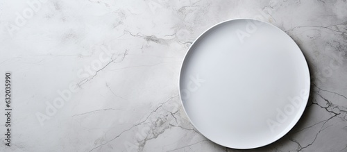 A white plate is placed on a white stone table, viewed from the top, with empty space around it.