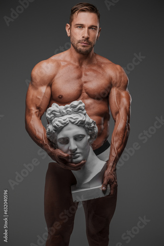 A hunky male model in underwear showcasing a captivating pose with an ancient Greek bust on a grey backdrop photo