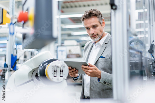 Businessman with tablet at assembly robot in a factory