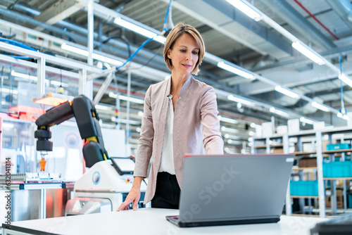 Businesswoman in a modern factory hall using laptop