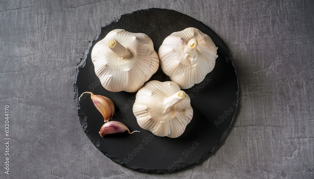 still life arrangement for overhead shot of Three whole garlic bulbs grouped on black stone plate
