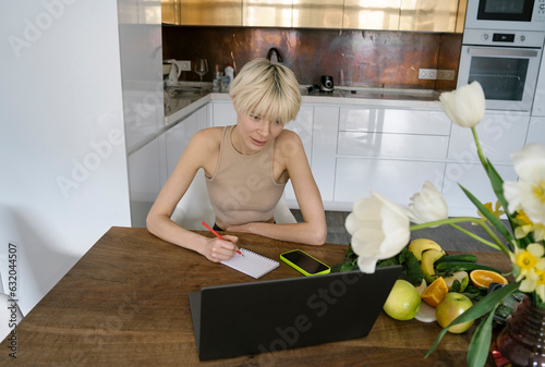 Curious nutritionist talking diet notes from laptop in kitchen photo