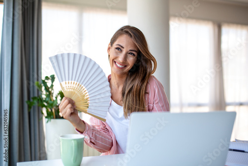 Photos A young woman sweats profusely while working on her laptop in an overheated home office