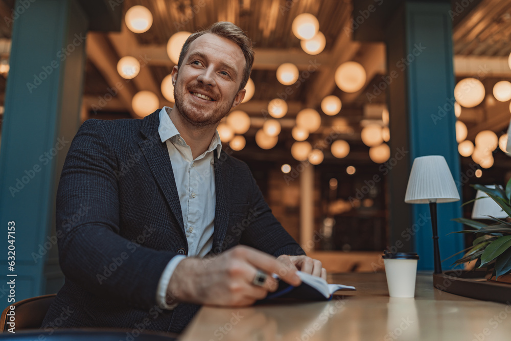 Fototapeta premium Smiling businessman holding a notepad and drinking coffee during working day in modern coworking