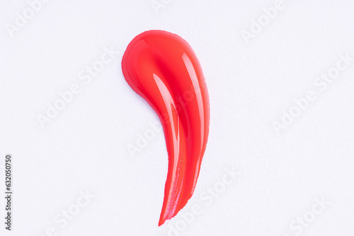Deep red swatch of lip gloss, cosmetic product stroke or paint, macro. Swatches of red lipgloss or paint on white paper background.