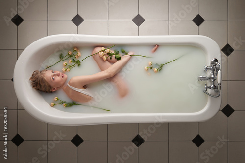 Directly above view of attractive blond woman relaxing in bathtub filled with milk and roses and looking at camera mysteriously    photo