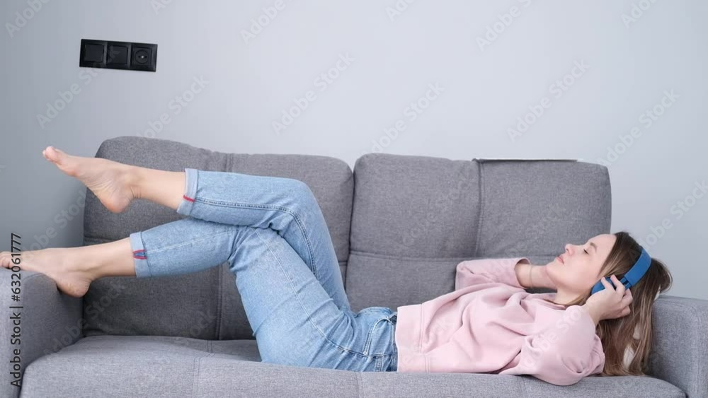 Calm happy young woman wearing wireless headphones, lying on sofa with closed eyes, listening to favorite music using mobile online player, enjoy calm mood in headphones at home Calm happy young woman wearing wireless headphones, lying on sofa with closed eyes, listening to favorite music using mobile online player, enjoy calm mood in headphones at home