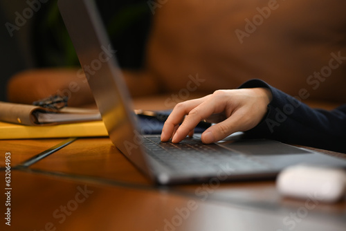 Select focus on hand of man freelancer sitting in living room working remotely, surfing internet on laptop