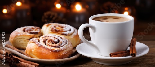 Cinnamon buns, which are freshly baked rolls filled with spices and cocoa, are served with coffee or cappuccino on a white plate, placed on a wooden background. They are commonly enjoyed as a Swedish
