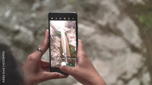 Young woman holding a phone and taking pictures of Nydri waterfall. Slow motion of woman hands holding a phone and taking pictures of waterfall photo