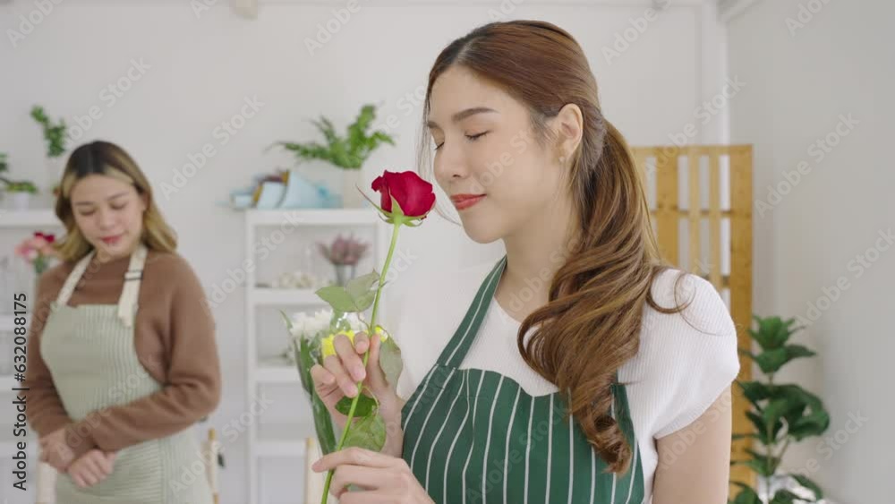 Beautiful Asian florist smelling red roses working in her shop. Small business, Owner business.