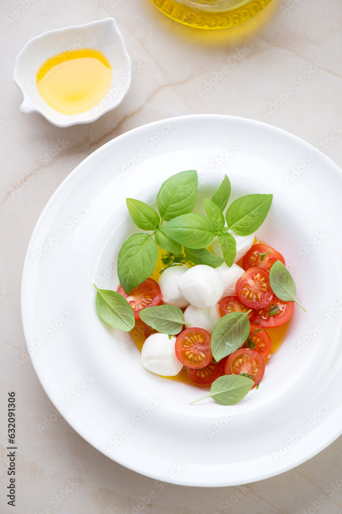 Caprese with mini mozzarella, red cherries and green basil in a white plate, vertical shot on a beige granite background, elevated view Caprese with mini mozzarella, red cherries and green basil in a white plate, vertical shot on a beige granite background, elevated view