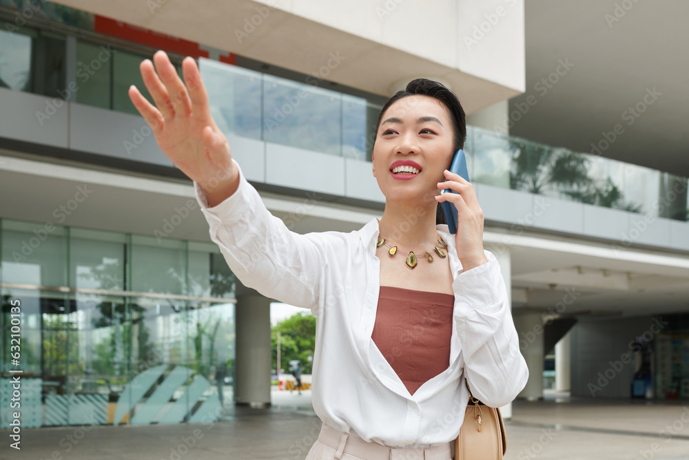 Fototapeta premium Joyful Asian businesswoman talking on phone and catching taxi car