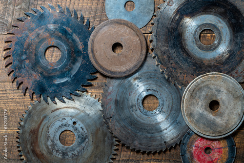 Old circular saw blades and emery wheels on wooden table, closeup, top view. Carpentry tools, sawing and grinding equipment photo