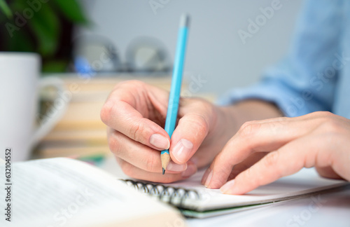 A young girl student prepares her homework and writes notes in a notebook. Close-up. Selective focus.