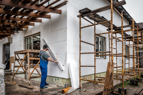 Insulation of the house with polyfoam. The worker is checking with the construction level the accuracy of the installation of polystyrene board on the facade