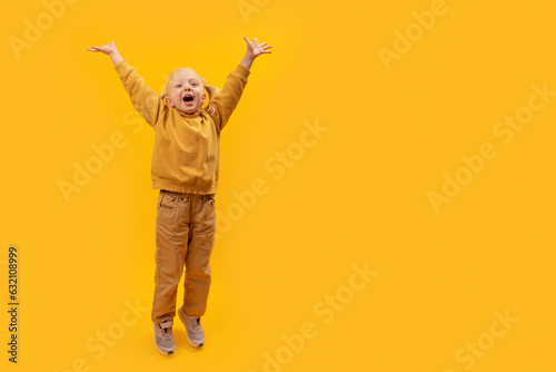 Happy cheerful preschool girl raised her hands up and laughed. Child on bright yellow background. Copy space, mock up