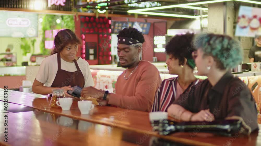 Young black guy talking with diverse girlfriends and paying with smartwatch for dinner on food court Young black guy talking with diverse girlfriends and paying with smartwatch for dinner on food court