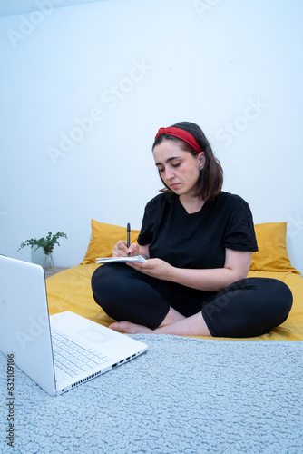 Aprendizaje en la comodidad: Mujer dedicada estudiando con su portátil y tomando apuntes en la cama