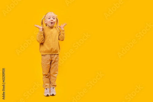 Girl is screams or surprised. Space for text, mock up. Full-length portrait of little girl in yellow suit on yellow background