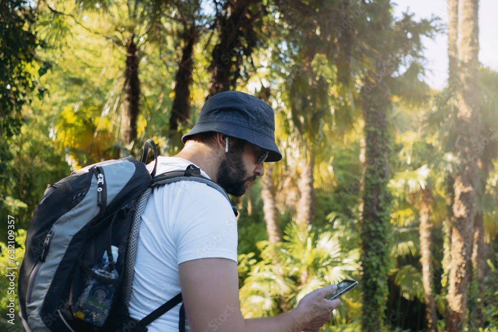millenial bearded tourist man wearing bucket hat, with backpack and earpods using smartphone for navigation millenial bearded tourist man wearing bucket hat, with backpack and earpods using smartphone for navigation