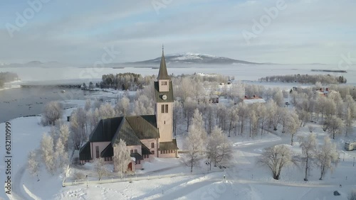 Drone shot orbiting a church during winter with surrounding pinetrees and hills and frozen lakes in the background in Northern Sweden. photo