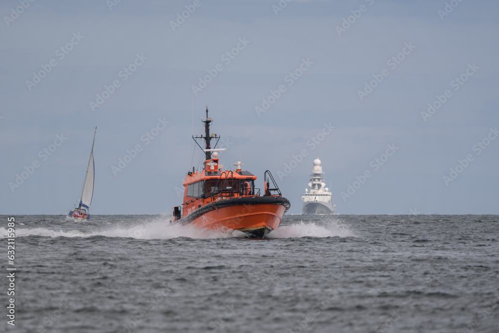 PILOT BOAT - An orange high-speed motorboat is maneuvering against the backdrop of a warship PILOT BOAT - An orange high-speed motorboat is maneuvering against the backdrop of a warship