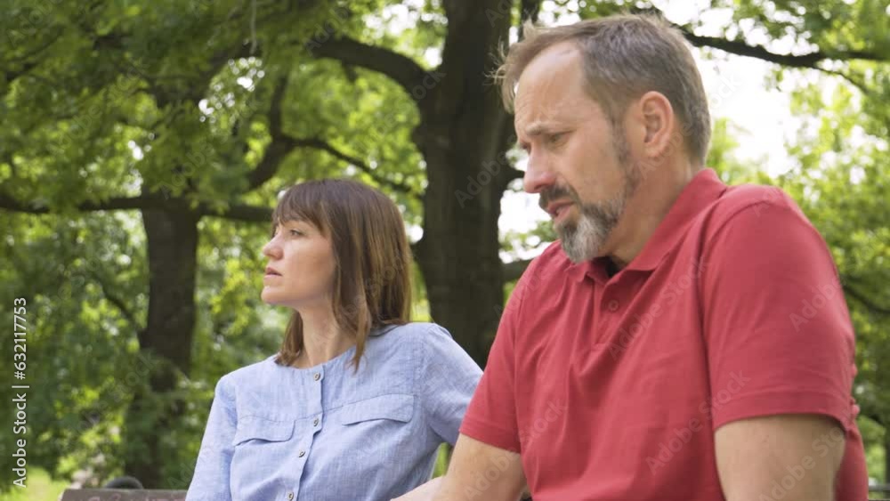 A middle-aged Caucasian couple argues in a park - she's angry, he's frustrated A middle-aged Caucasian couple argues in a park - she's angry, he's frustrated