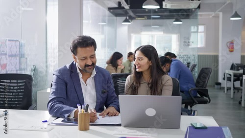 Two modern happy Indian Asian female and male corporate entrepreneurs sitting together busy discussing ideas and writing it down the sales target on a paper while working in diverse start up business