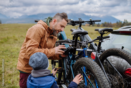 Littlle boy helping father attache a bicycle on bike carrier. photo